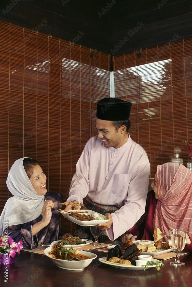 Man passing a plate of satay to his friends Man passing a plate of satay to his friends