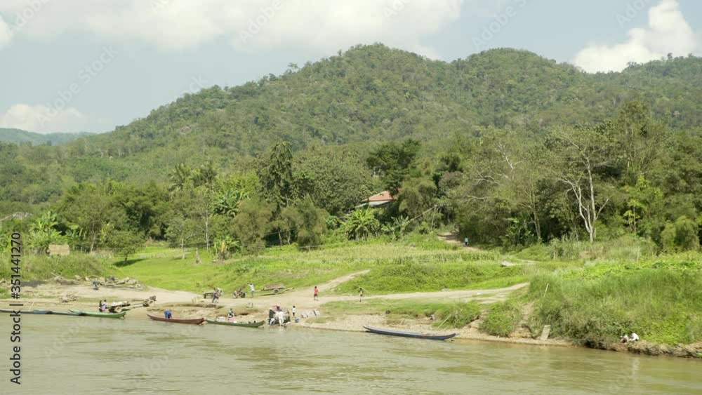 Panning shot of people and boats at riverbank against mountain range during summer - Chiang Rai, Thailand Panning shot of people and boats at riverbank against mountain range during summer - Chiang Rai, Thailand