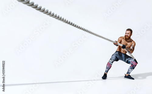 Strong man pulling rope. Photo of sporty man on white background. Strength  and motivation. Side view. Full length Stock Photo