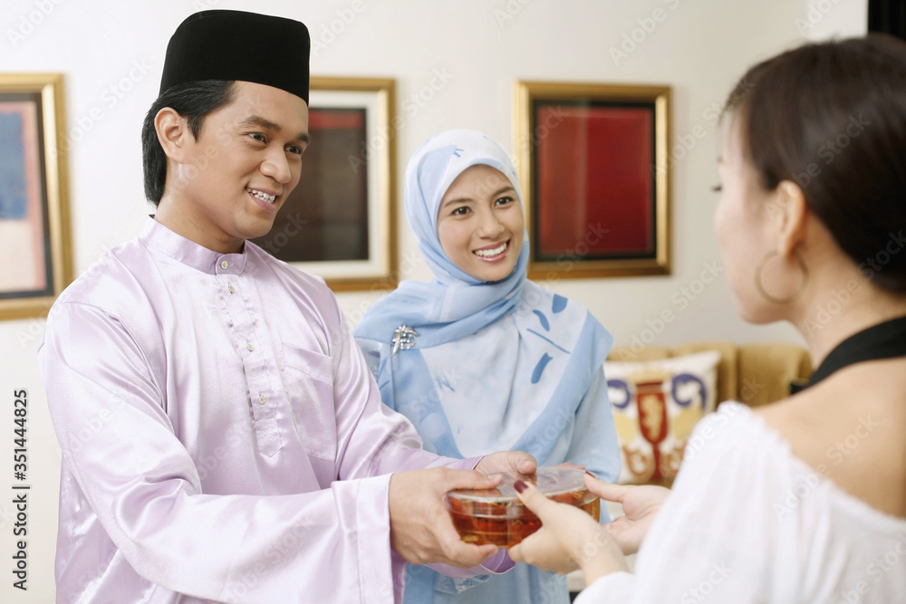 Woman giving man a box of traditional cookies during Hari Raya Woman giving man a box of traditional cookies during Hari Raya