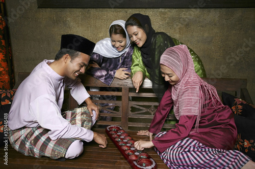 Man and woman playing congkak, the rest watching photo