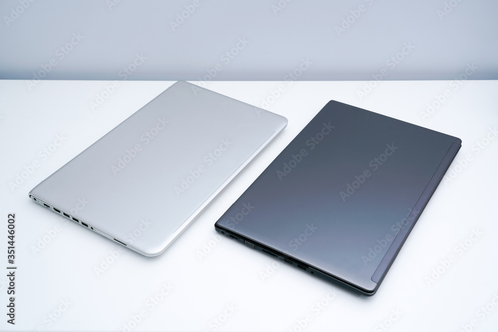 A dark grey laptop and a silver laptop are on the white desk A dark grey laptop and a silver laptop are on the white desk