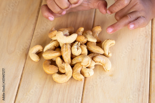 Many Roasted salted cashew nuts and kid hand on wooden background