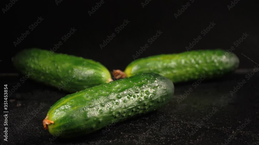 Sprinkling green cucumbers on dark table with water Sprinkling green cucumbers on dark table with water