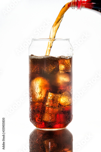 Cold carbonated drink being poured over ice cubes in a can shaped glass
