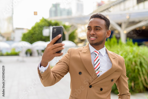 Happy young handsome African businessman taking selfie in the city