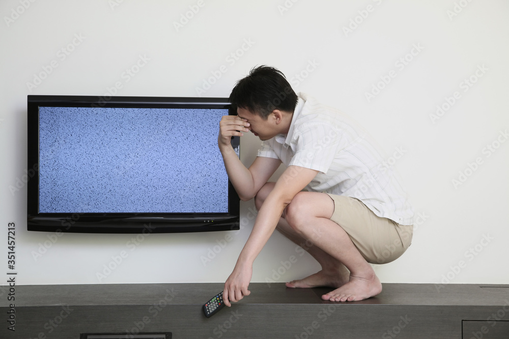 Man squatting beside a ruined television with hand on head Man squatting beside a ruined television with hand on head