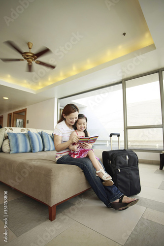 Mother and daughter reading book together while waiting at the hotel lobby