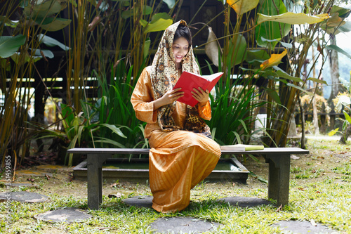 Woman in traditional clothing reading book in the house compound