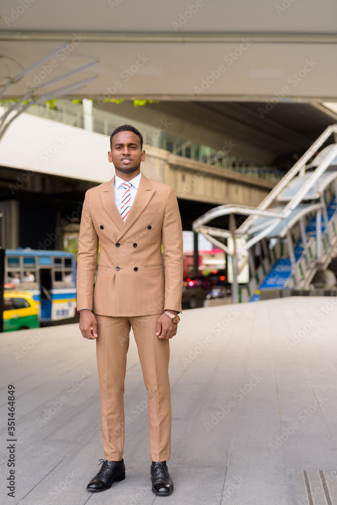 Full body shot of happy young handsome African businessman smiling in the city streets outdoors Full body shot of happy young handsome African businessman smiling in the city streets outdoors
