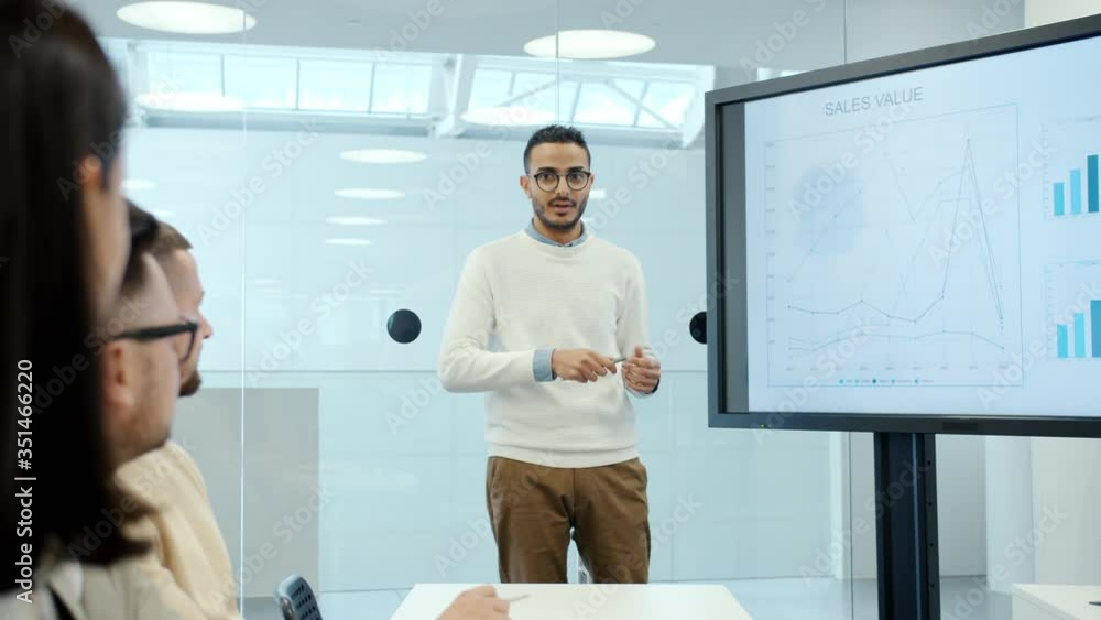Young Arabian businessman is giving presentation about sales using digital whiteboard in office explaining financial strategies to group of people.