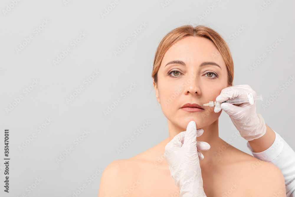 Woman receiving filler injection against grey background Woman receiving filler injection against grey background