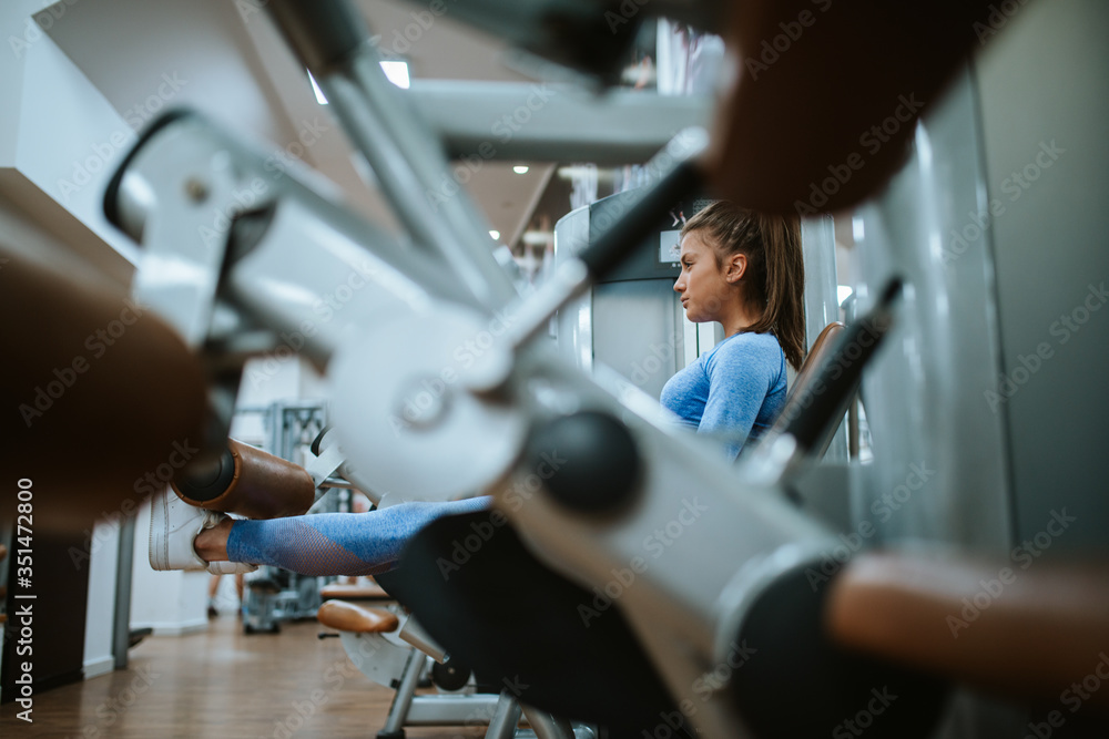 An attractive young caucasian girl in blue sports equipment on a leg machine in the gym
