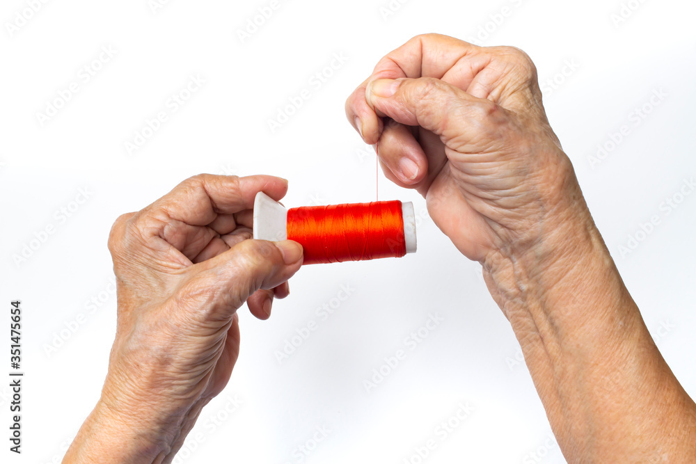 Senior woman hands spinning to orange thread roll on isolated white background, Close up and macro shot Asian body part, Hobby, About Tailor Processing concept Senior woman hands spinning to orange thread roll on isolated white background, Close up and macro shot Asian body part, Hobby, About Tailor Processing concept