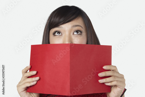 Woman in traditional clothing covering her mouth with a greeting card © ImageHit