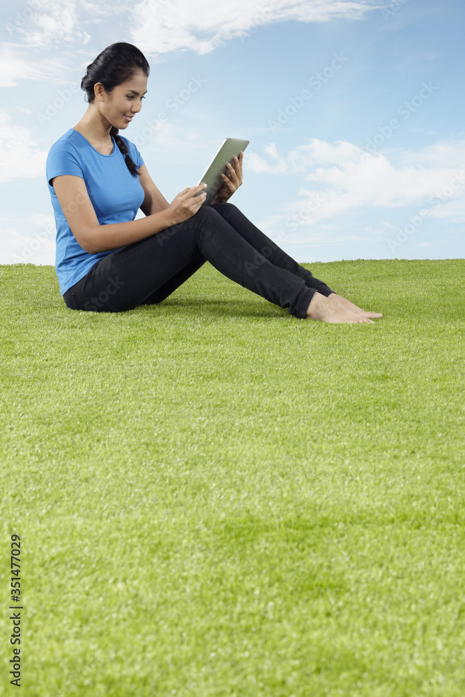 Young woman sitting on grass, reading from digital tablet Young woman sitting on grass, reading from digital tablet