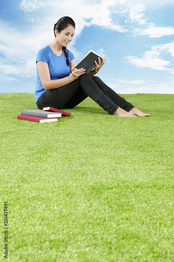 Young woman sitting on grass reading a book Young woman sitting on grass reading a book