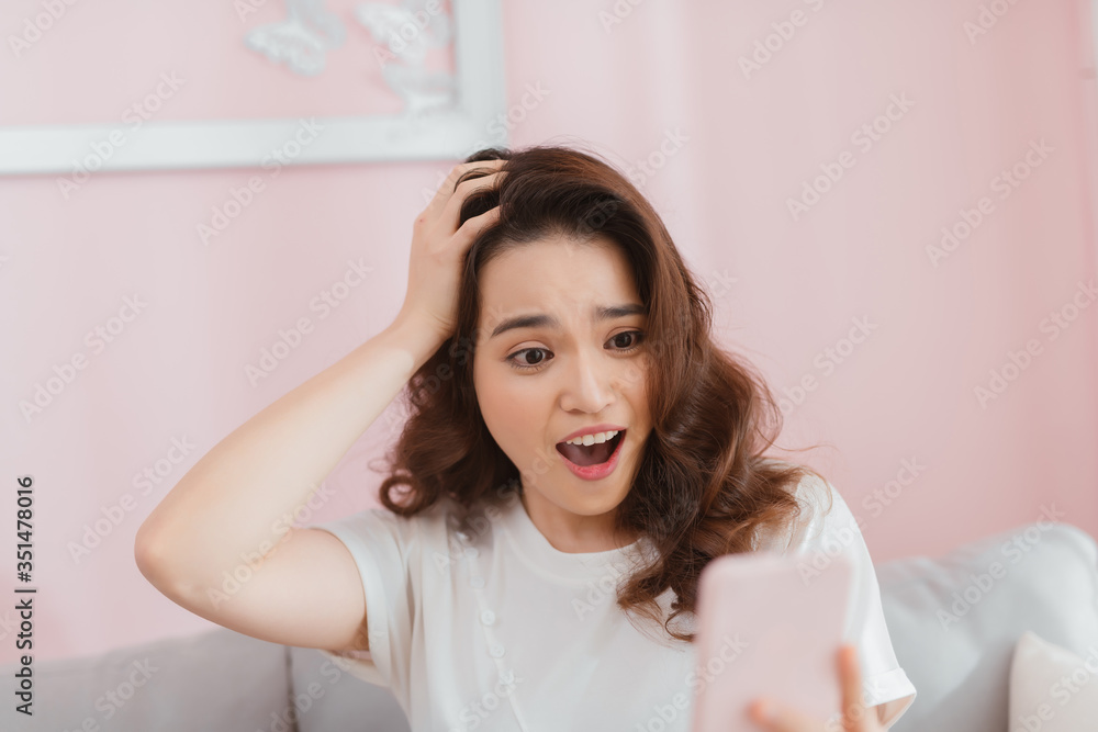 Surprised asian woman looking at her smartphone at home in the living room Surprised asian woman looking at her smartphone at home in the living room