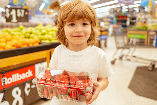 Happy little customer boy with strawberry, shopping at supermarket, grocery store. A boy is shopping in a supermarket. Supermarket, Shopping with Child. © Volodymyr