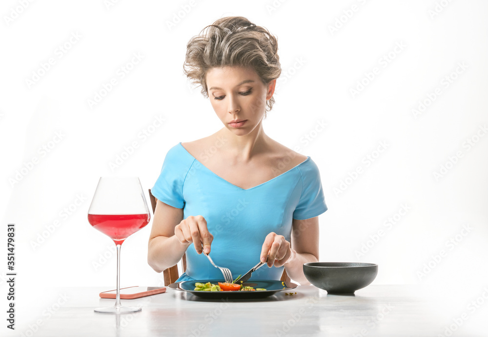 Beautiful woman sitting at the table and is eating vegetable salad. White background Beautiful woman sitting at the table and is eating vegetable salad. White background