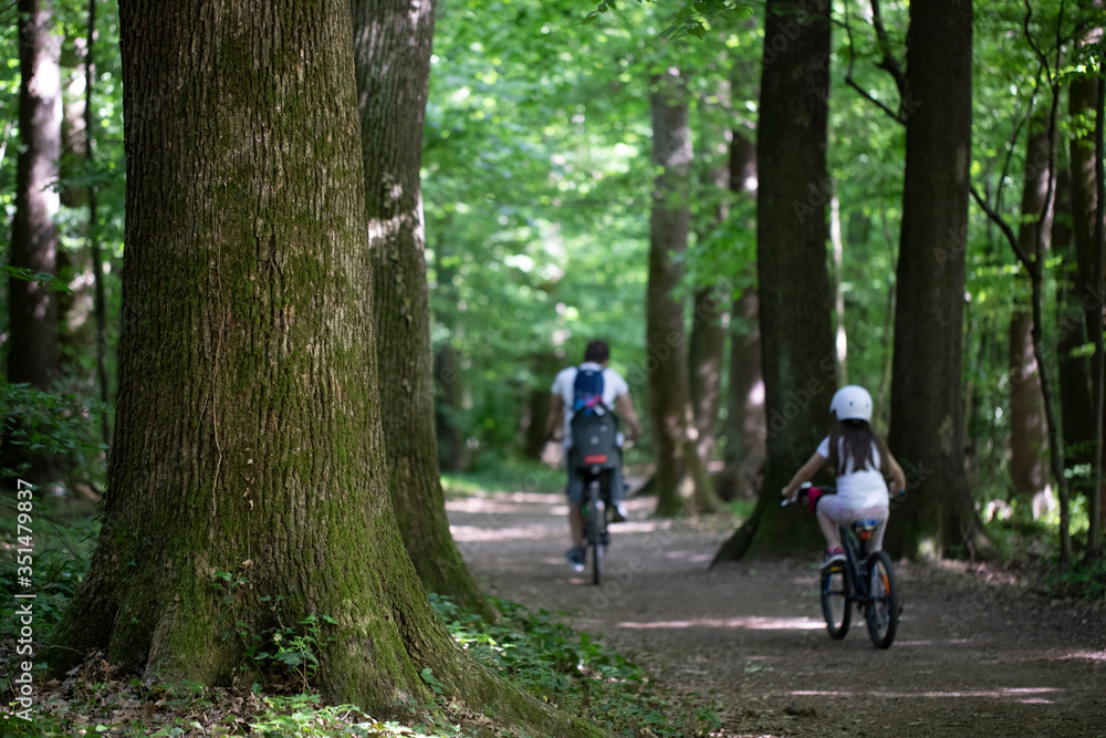 Dad and his dauther cycling down a forest path
