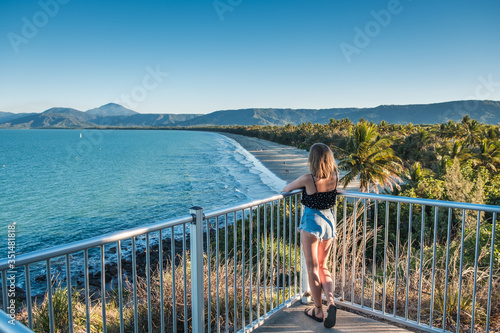 Attractive young girl standing on viewing platform, looking on beach surrounded by mountains and trees in Australia