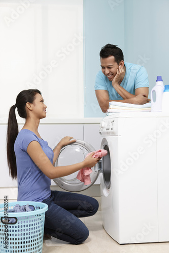 Woman putting clothes into washing machine, man watching