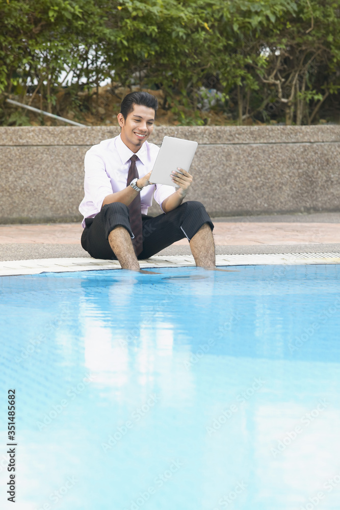 Young businessman using digital tablet by the swimming pool