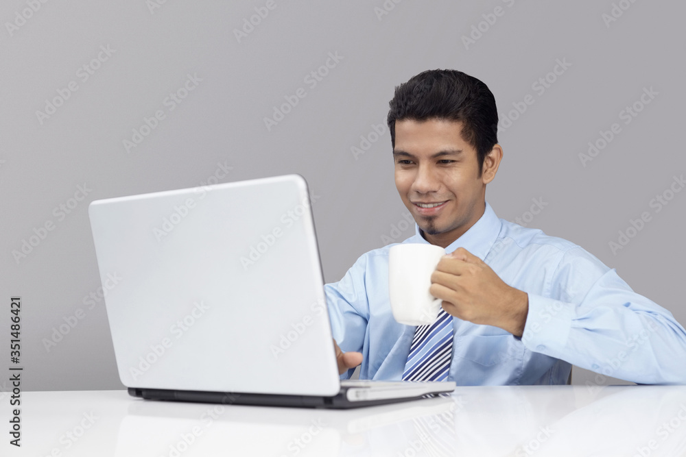 Young businessman enjoying a cup of coffee while working on laptop Young businessman enjoying a cup of coffee while working on laptop