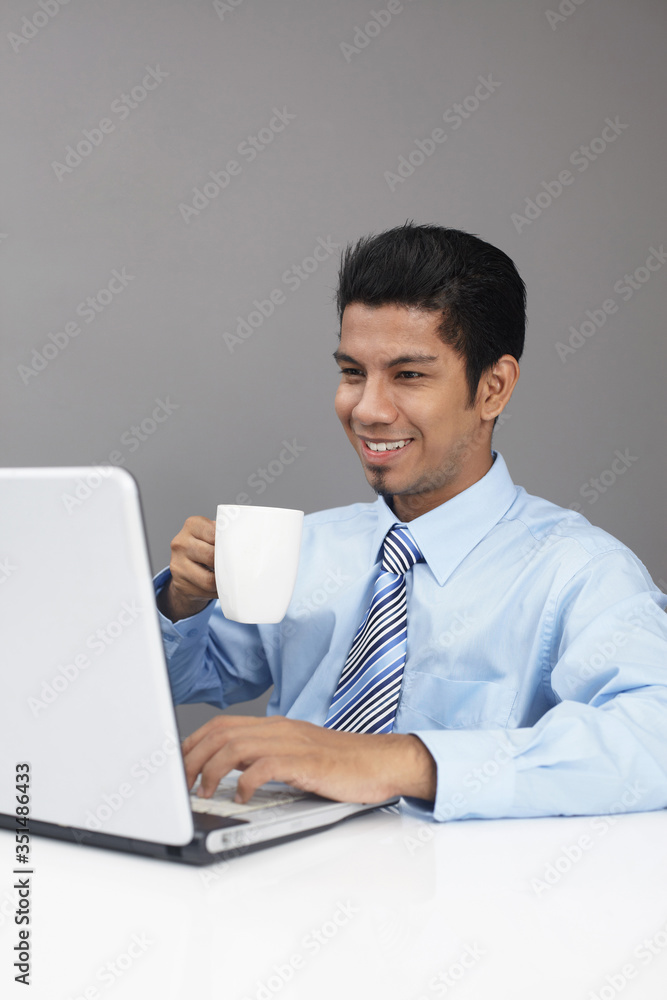 Young businessman enjoying a cup of coffee while working on laptop Young businessman enjoying a cup of coffee while working on laptop