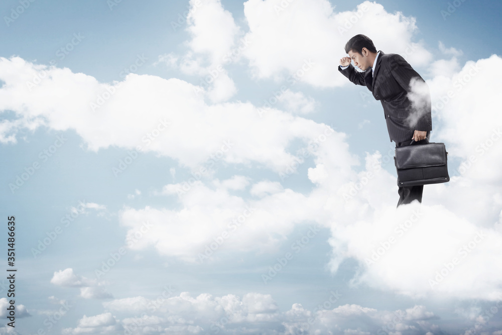 Young businessman standing on clouds, looking below Young businessman standing on clouds, looking below