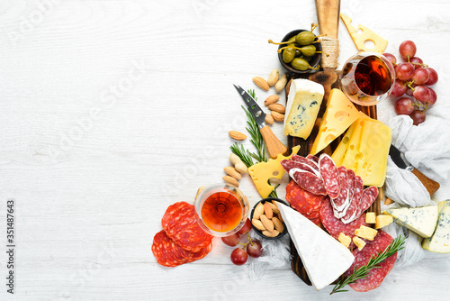 Italian antipasti wine snacks set. Cheese variety, salami and grapes on a white wooden background. Italian cuisine. Top view. Free space for your text. photo