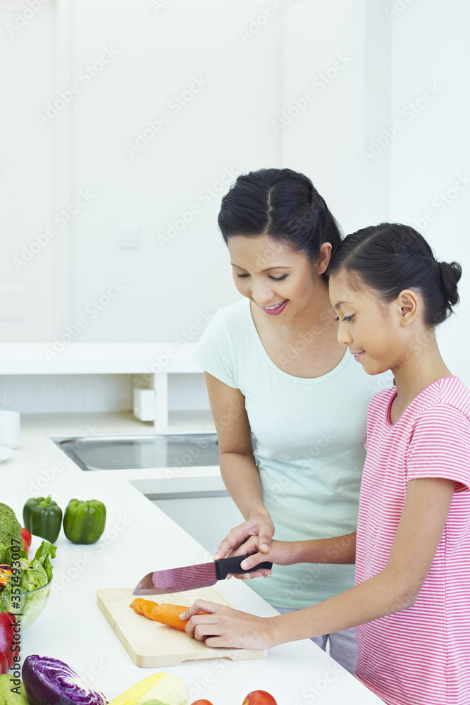Woman teaching girl to cut vegetables