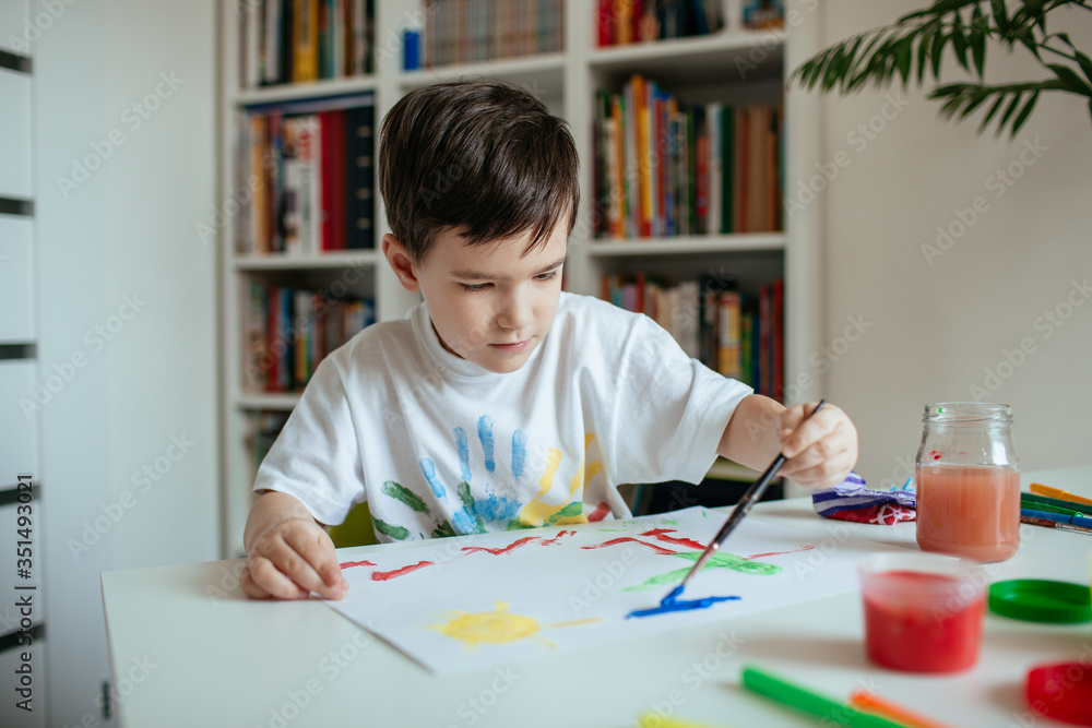 Left handed cute preschooler boy painting picture.