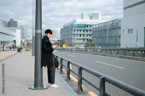 Young asian man waiting for bus and taxi on sidewalk