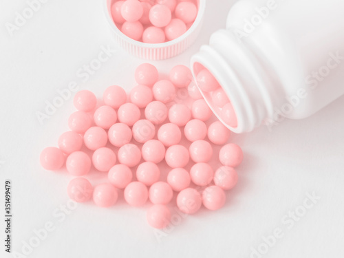 Vitamins. Antiviral drug tablets. Round pink healthy pills and pill bottle on white background. Homeopathic globules, alternative homeopathy medicine. Minimalistic concept
