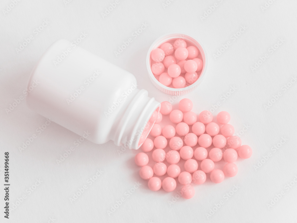 Vitamins. Antiviral drug tablets. Round pink healthy pills and pill bottle on white background. Homeopathic globules, alternative homeopathy medicine. Minimalistic concept Vitamins. Antiviral drug tablets. Round pink healthy pills and pill bottle on white background. Homeopathic globules, alternative homeopathy medicine. Minimalistic concept