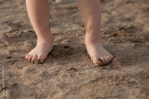 Small children's feet stand on the sand in summer.