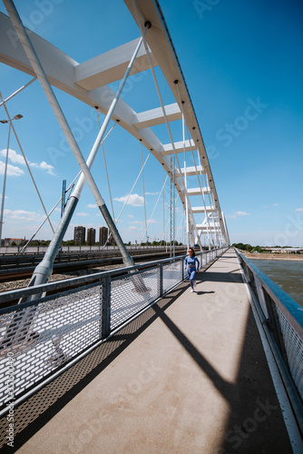 A young beautiful caucasian girl in blue sports equipment is running on the bridge. Training in nature