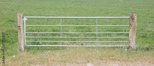 Metal fence and farm gate leading into grassy field