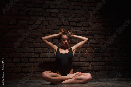 Girl in black swimsuit does yoga against the background of a brick wall