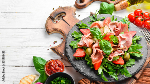 Photos Salad of arugula, prosciutto, strawberries and capers on a black stone plate