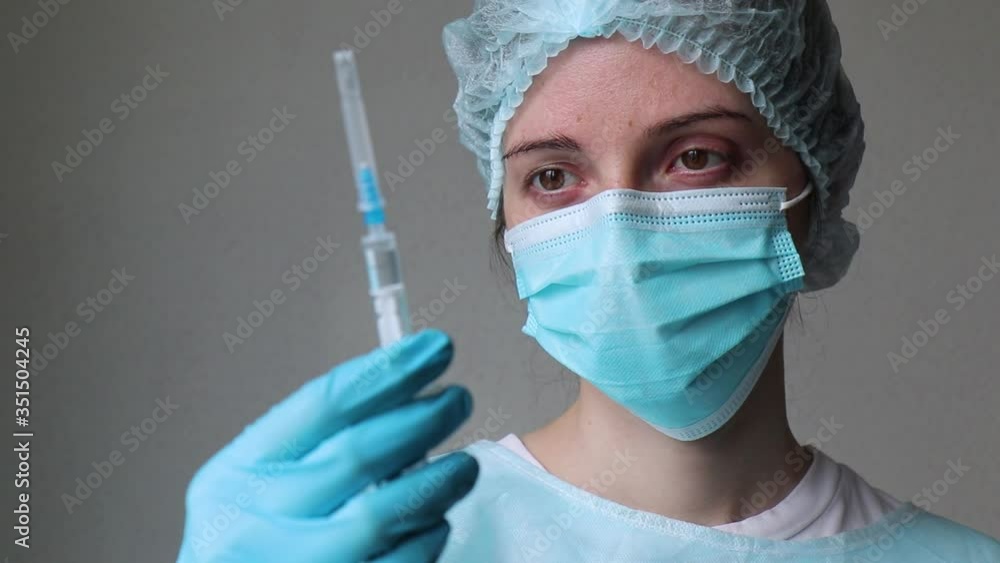 doctor in a medical mask looks at the syringe, removes the cap from it and prepares to inject doctor in a medical mask looks at the syringe, removes the cap from it and prepares to inject