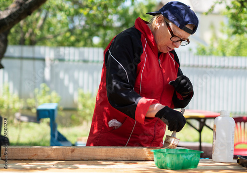 Senior Caucasian woman covers wood with an antiseptic to protect against rot and fire