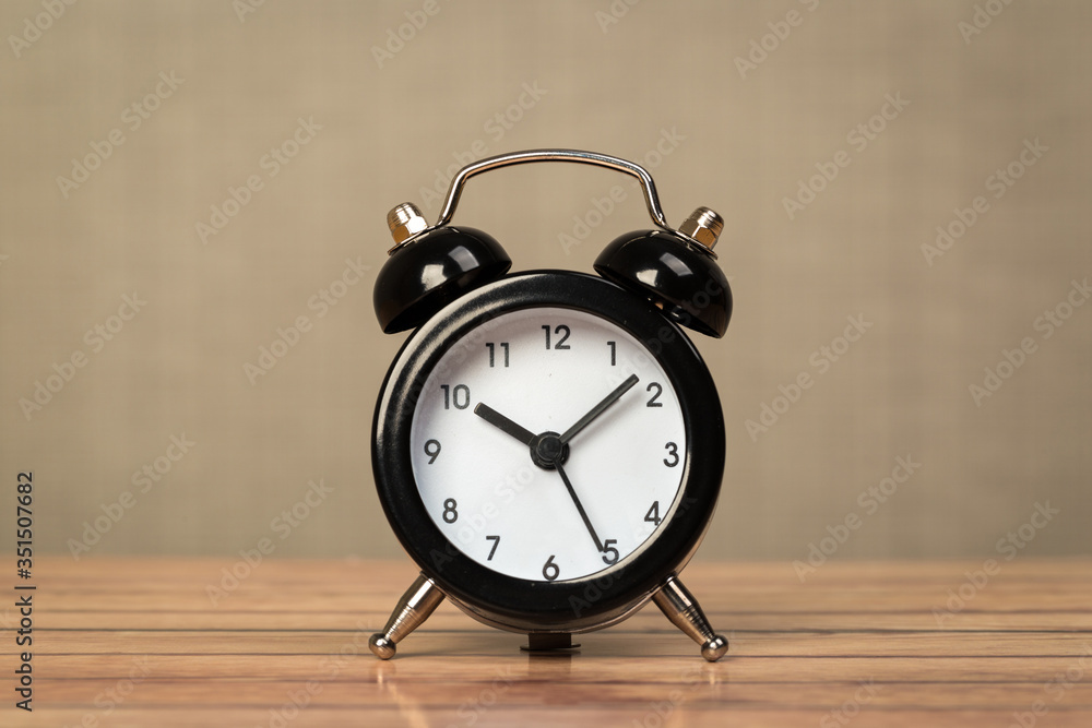 Black retro alarm clock with bells on a wooden table, daily routine concept.