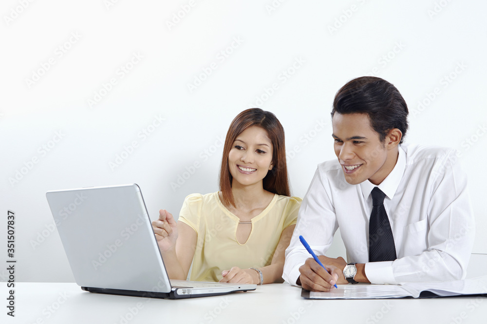 Cheerful businessman and businesswoman working on laptop together Cheerful businessman and businesswoman working on laptop together