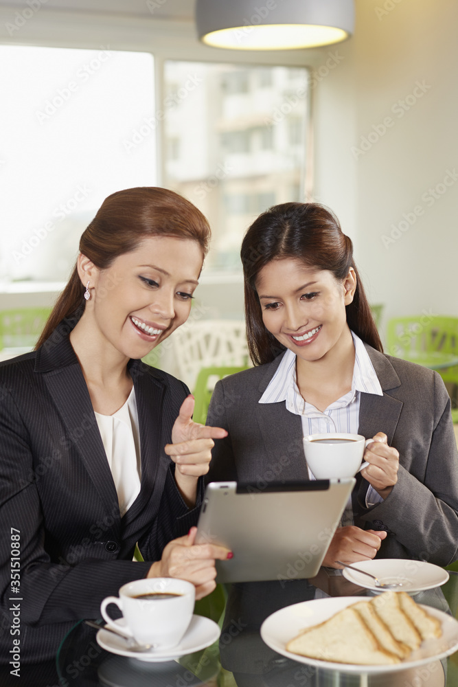 Businesswomen using digital tablet while having a drink Businesswomen using digital tablet while having a drink