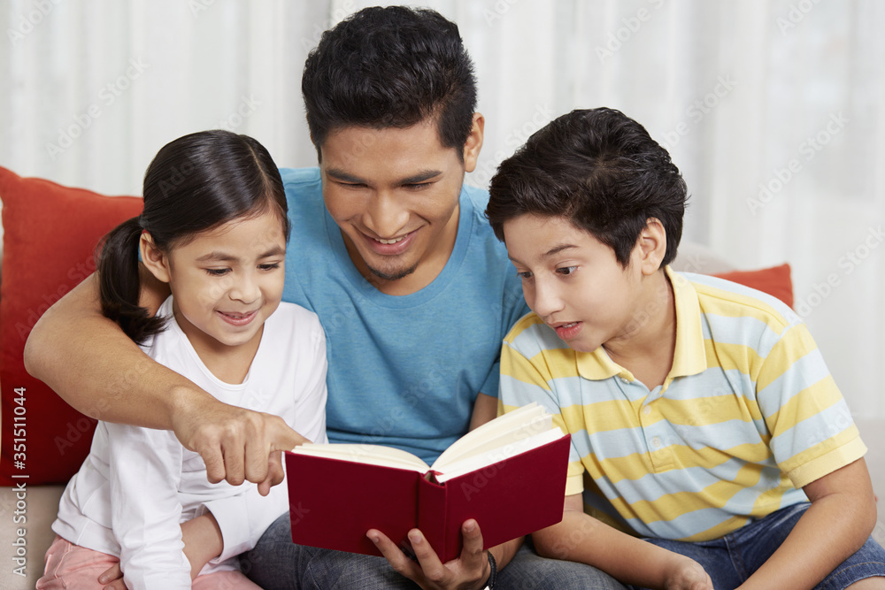 Fototapeta premium Father reading a book with his children