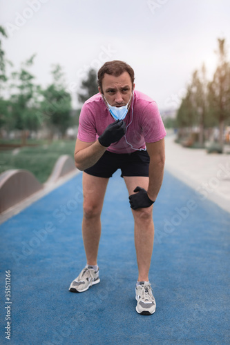 Fototapeta Naklejka Na Ścianę i Meble -  Sportsman with medical mask and gloves, smartphone and earbuds working out, jogging in urban surroundings.