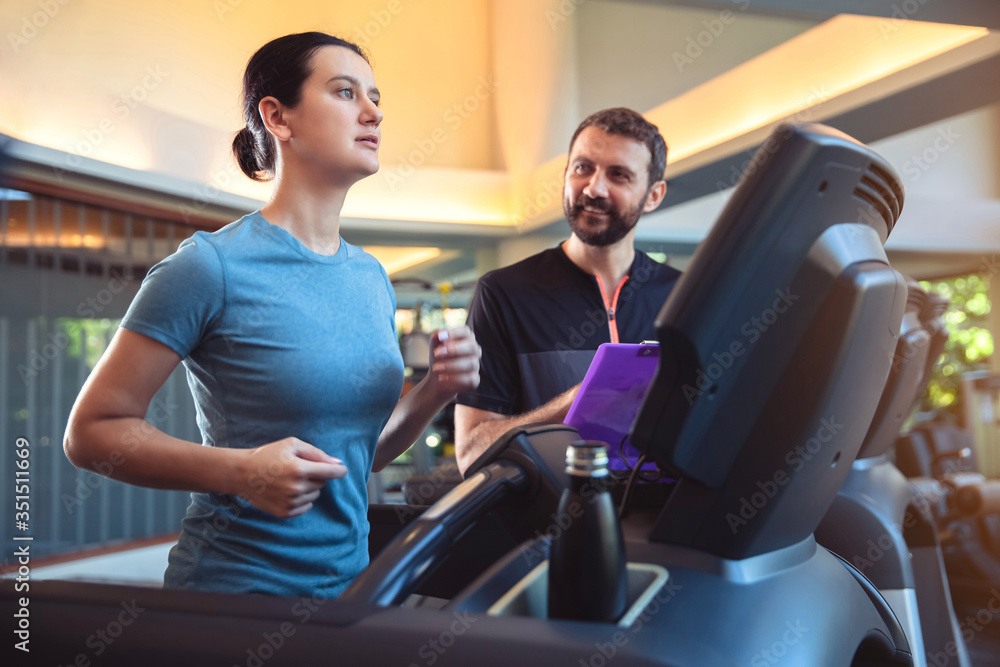 Personal trainer working with client in gym. Trainer man helping woman with her work out